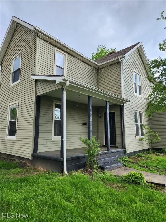 rear view of property featuring a lawn and covered porch