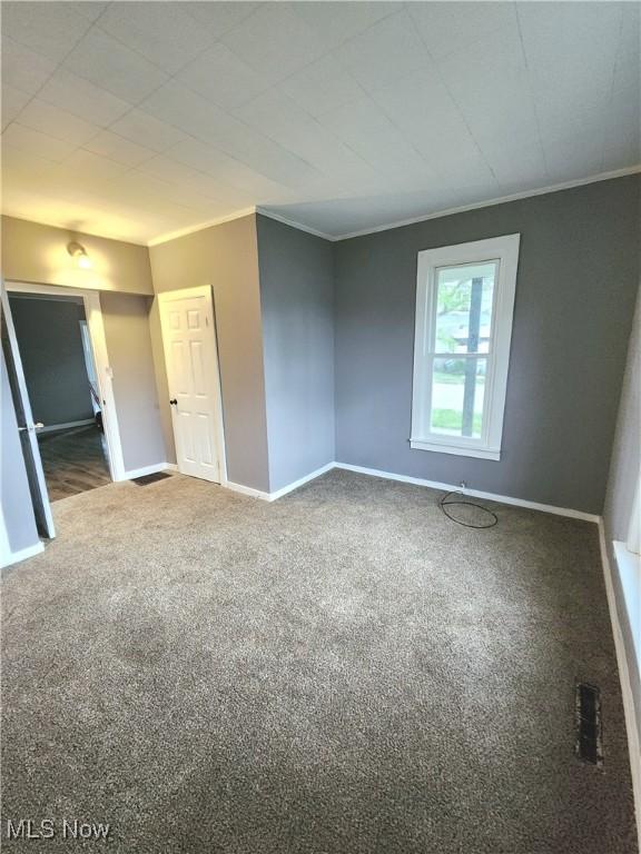 carpeted spare room featuring crown molding and baseboards