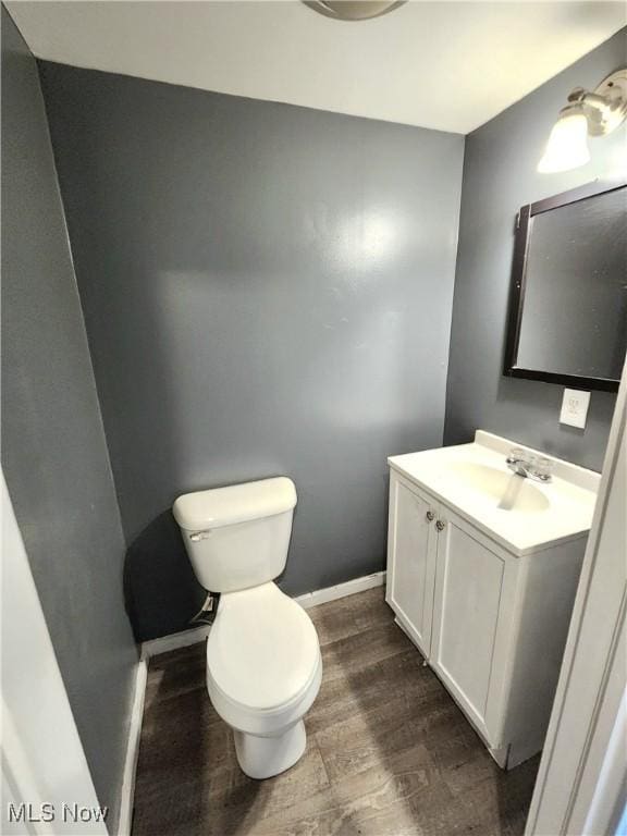 half bath with toilet, baseboards, wood finished floors, and vanity