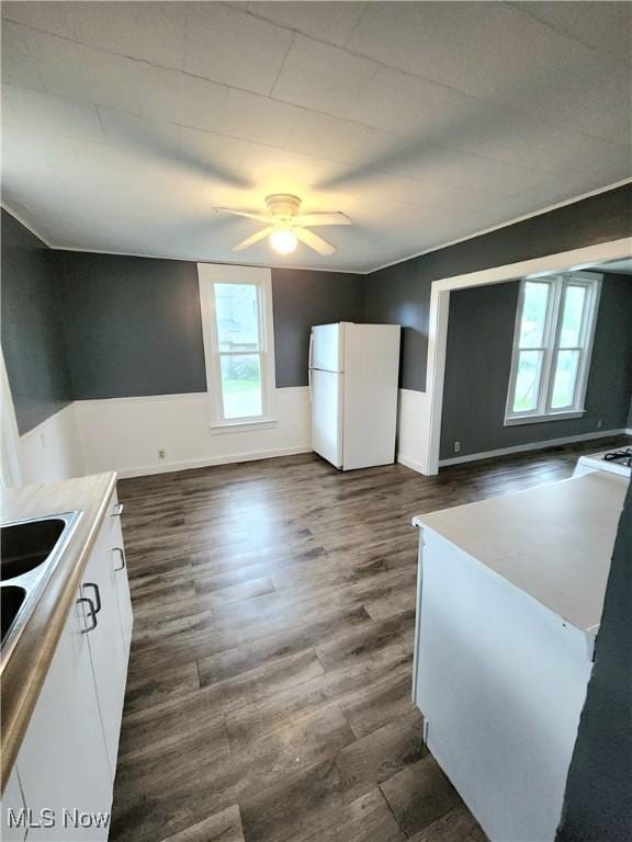 kitchen with a sink, freestanding refrigerator, dark wood finished floors, ceiling fan, and white cabinets