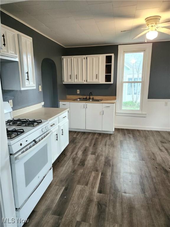 kitchen with white gas range oven, a sink, white cabinetry, dark wood-type flooring, and arched walkways