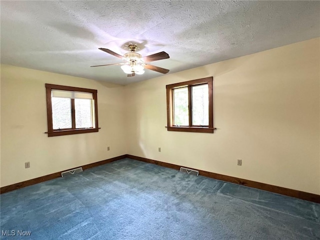 spare room featuring ceiling fan, dark carpet, visible vents, and a healthy amount of sunlight