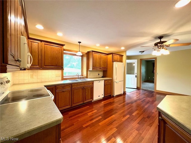 kitchen featuring a sink, white appliances, brown cabinets, backsplash, and dark wood-style floors