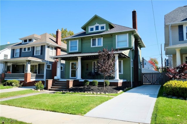 american foursquare style home featuring covered porch, concrete driveway, a chimney, and a front yard