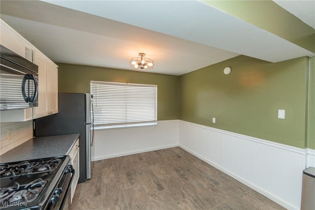 3019 Clague Rd, North Olmsted, OH 44070 - kitchen featuring an inviting chandelier, dark countertops, wainscoting, range with gas stovetop, and black microwave