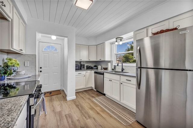 kitchen featuring a sink, stainless steel appliances, light wood-style flooring, white cabinetry, and decorative backsplash