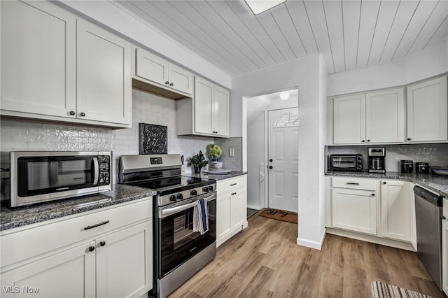 kitchen with stainless steel appliances, dark stone counters, light wood-type flooring, decorative backsplash, and white cabinets