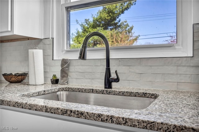 room details featuring a sink, tasteful backsplash, light stone counters, and white cabinets