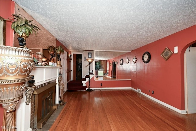 unfurnished living room with hardwood / wood-style flooring, a textured ceiling, arched walkways, and stairs