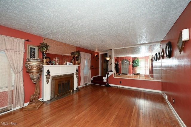 unfurnished living room with a fireplace with flush hearth, a textured ceiling, baseboards, and wood-type flooring
