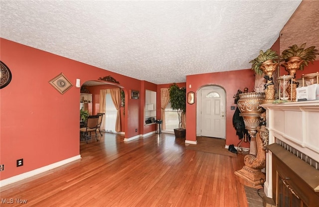foyer entrance with arched walkways, a fireplace, a textured ceiling, and hardwood / wood-style flooring