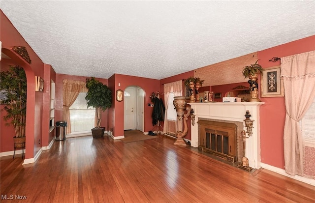 unfurnished living room featuring wood-type flooring, a textured ceiling, baseboards, arched walkways, and a glass covered fireplace