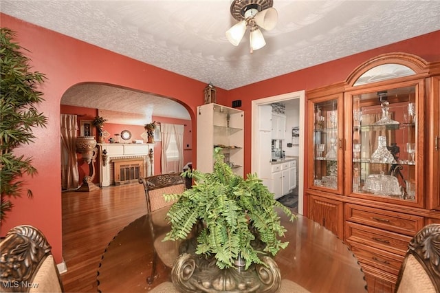 dining area featuring a textured ceiling, arched walkways, a fireplace with flush hearth, and wood finished floors
