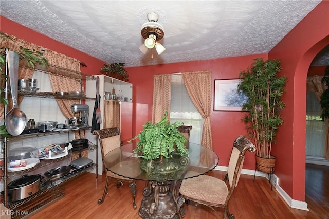 dining space featuring wood finished floors, a textured ceiling, ceiling fan, arched walkways, and baseboards