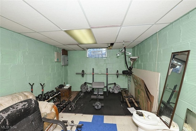 exercise area featuring a drop ceiling, tile patterned floors, concrete block wall, and electric panel