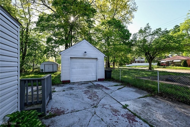 detached garage featuring driveway, fence, and a storage unit