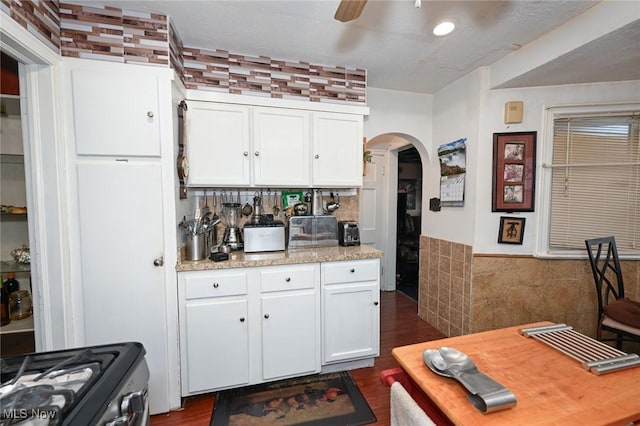 kitchen featuring tile walls, wainscoting, ceiling fan, arched walkways, and white cabinets