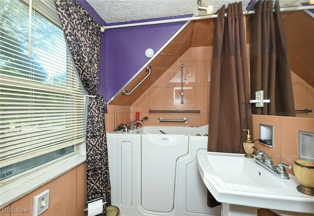 full bath with a textured ceiling, washer / dryer, and a sink
