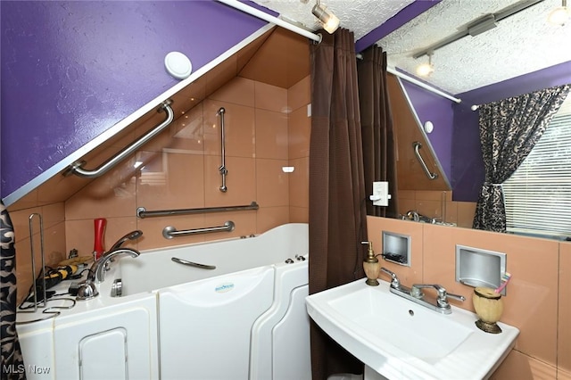 bathroom with a textured ceiling, shower / tub combo with curtain, and a sink