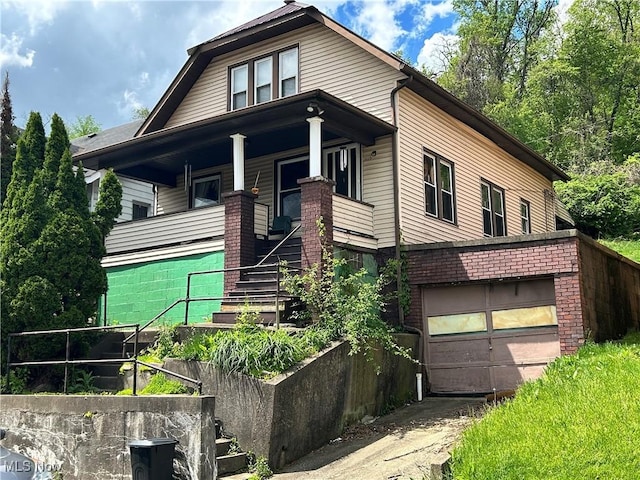 bungalow-style home with covered porch, stairs, driveway, a garage, and a vegetable garden