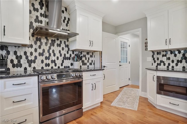 kitchen featuring light wood finished floors, wall chimney exhaust hood, oven, white cabinetry, and stainless steel range with gas cooktop
