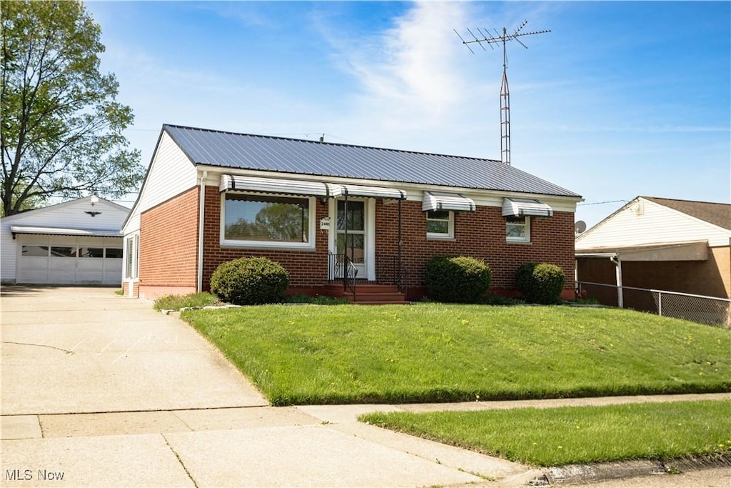 view of front of property featuring an outbuilding, brick siding, metal roof, a detached garage, and a front yard