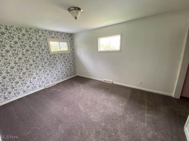 unfurnished room with dark colored carpet, baseboards, visible vents, and wallpapered walls