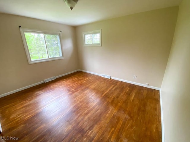 empty room with baseboards, visible vents, and dark wood-type flooring
