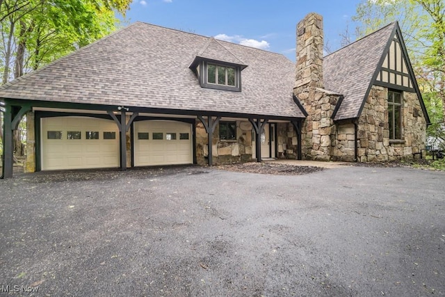 view of front of home with roof with shingles, stone siding, an attached garage, and a chimney
