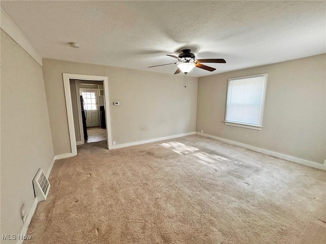 unfurnished room with light colored carpet, a textured ceiling, visible vents, ceiling fan, and baseboards