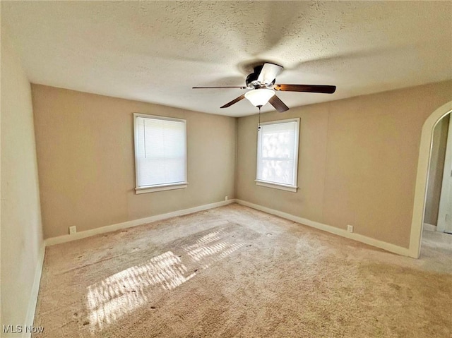 spare room with carpet, baseboards, ceiling fan, and arched walkways