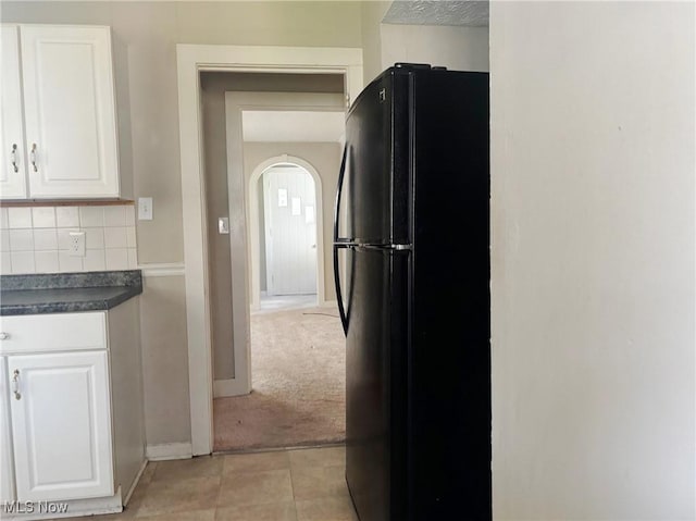 kitchen featuring freestanding refrigerator, dark countertops, white cabinets, arched walkways, and decorative backsplash