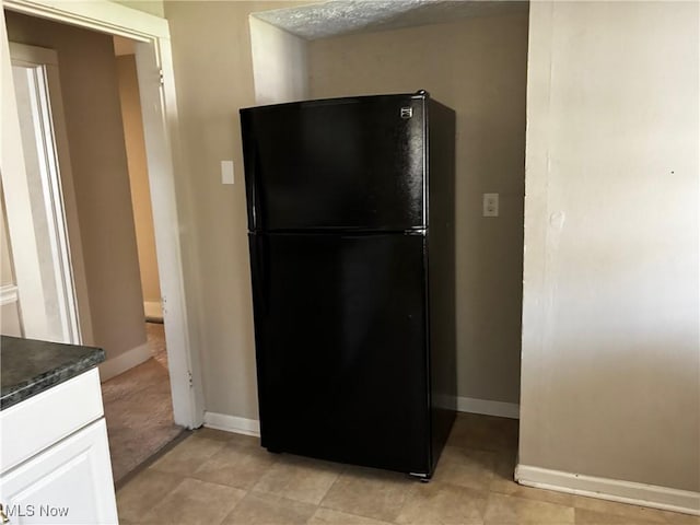kitchen with freestanding refrigerator, dark countertops, white cabinets, and baseboards