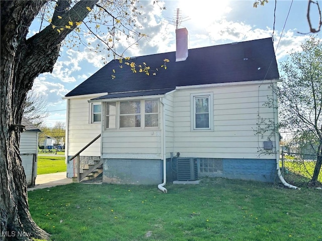 rear view of house with a lawn, a chimney, central AC unit, and fence