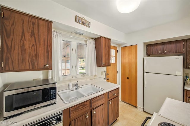 kitchen featuring a sink, stainless steel microwave, freestanding refrigerator, light tile patterned flooring, and light countertops
