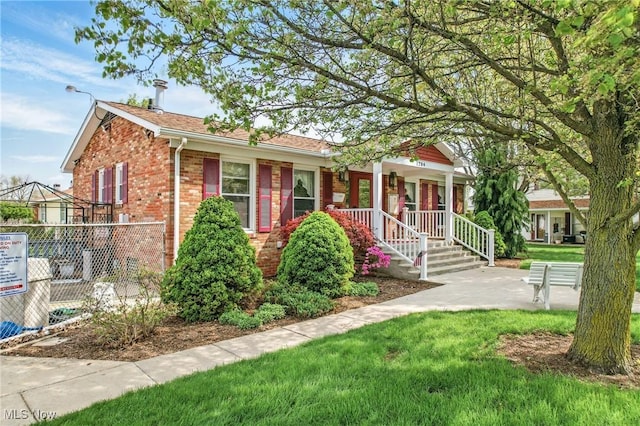 view of front facade with covered porch, fence, brick siding, and a front yard
