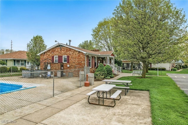 rear view of house featuring a lawn, brick siding, fence, a patio area, and a community pool