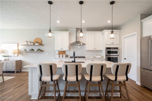 3991 Crestview Dr, Green, OH 44685 - kitchen featuring appliances with stainless steel finishes, wall chimney exhaust hood, light countertops, an island with sink, and dark wood-style floors