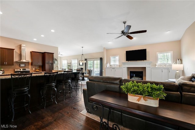 living area with recessed lighting, a ceiling fan, a glass covered fireplace, and dark wood finished floors