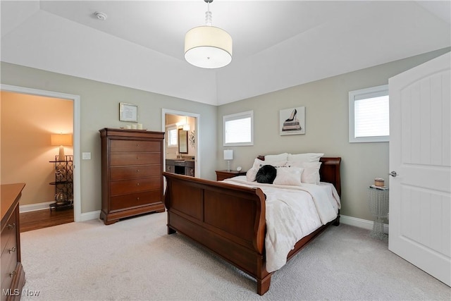 bedroom with ensuite bath, light colored carpet, and baseboards