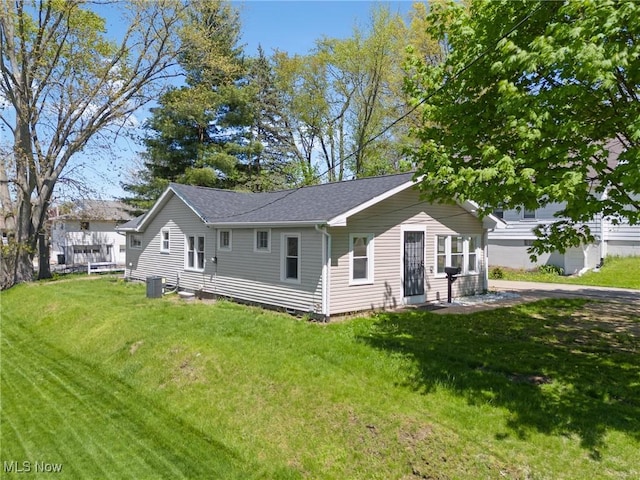 back of house with a yard, a shingled roof, and central AC unit