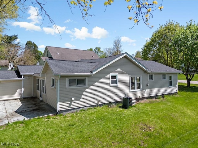 rear view of house with a yard, roof with shingles, central AC unit, and a patio area
