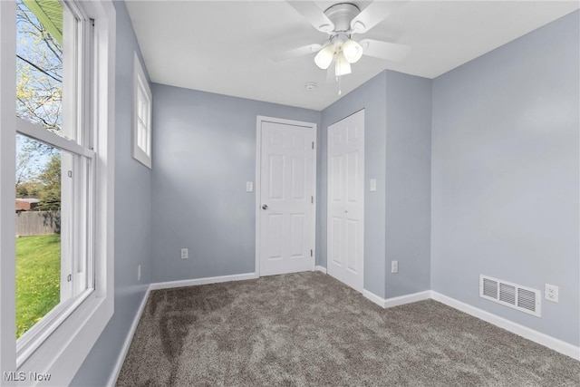 carpeted empty room featuring baseboards, a wealth of natural light, and visible vents