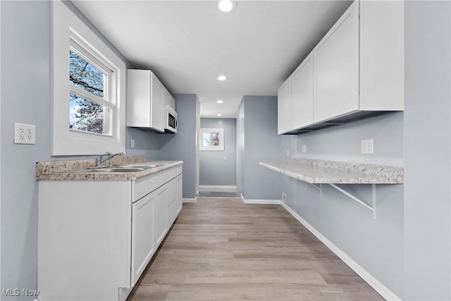 kitchen with a breakfast bar area, a sink, white cabinetry, white microwave, and light countertops
