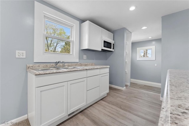 kitchen featuring baseboards, light countertops, white microwave, and a sink