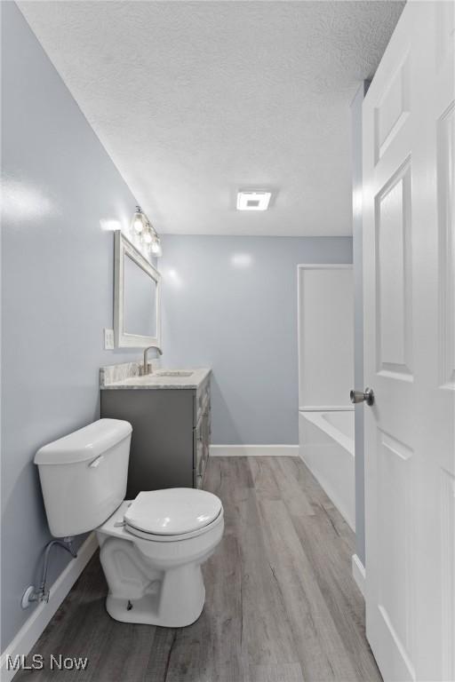 full bathroom featuring toilet, wood finished floors, vanity, a textured ceiling, and a tub