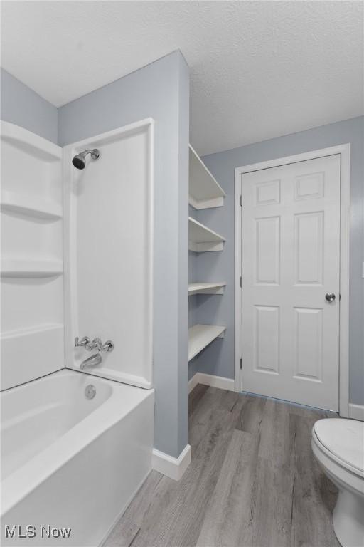 bathroom featuring shower / bathing tub combination, toilet, baseboards, and wood finished floors