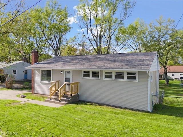 rear view of property with a yard, fence, a shingled roof, and a chimney