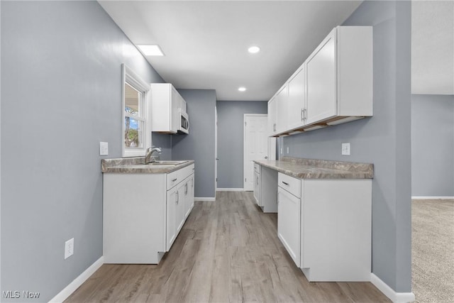 kitchen featuring baseboards, white microwave, white cabinets, and a sink