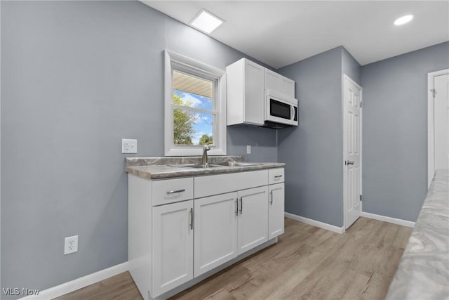 kitchen with light wood finished floors, white cabinetry, a sink, and white microwave